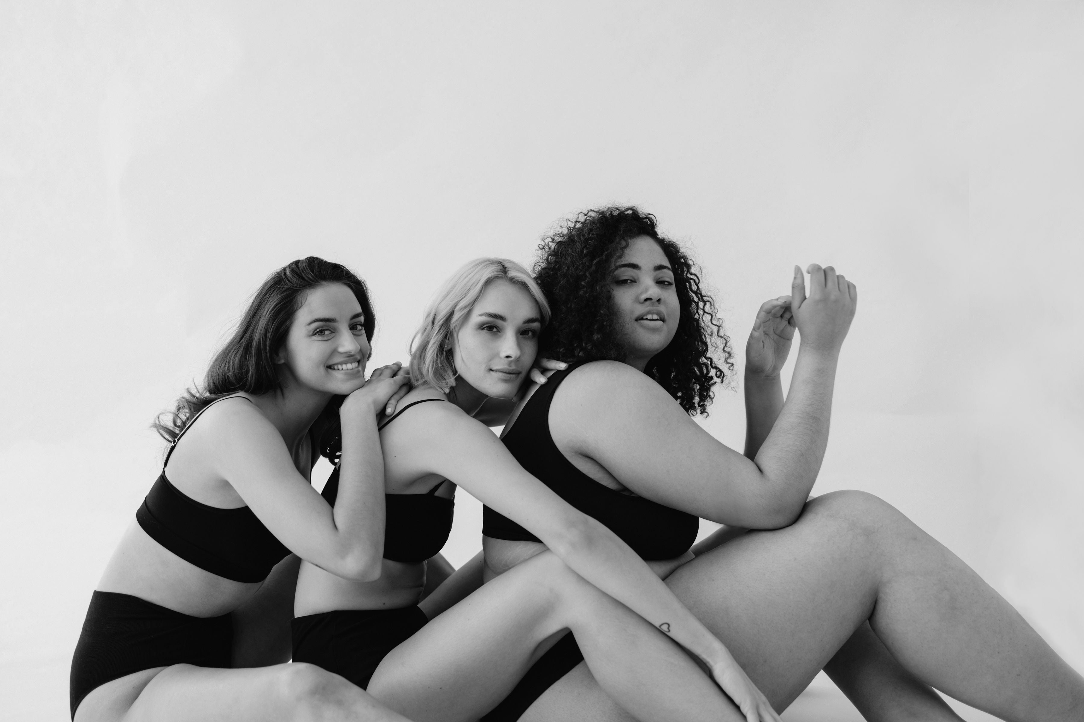 Drei Frauen sitzen auf dem Boden und sind aneinandergelehnt und bilden eine Community.