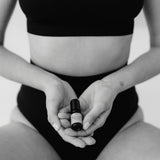 Eine Frau in schwarzer Unterwäsche hält ein schwarzes Fläschchen mit Aromaöl in den Händen.